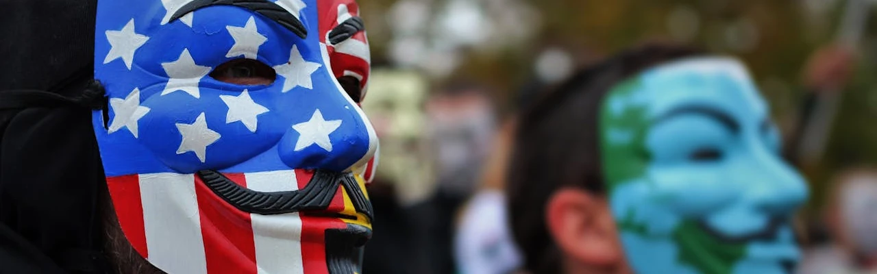 Dues persones amb màscarés de Guy Fawkes, una d’elles amb la bandera americana, en una manifestació
